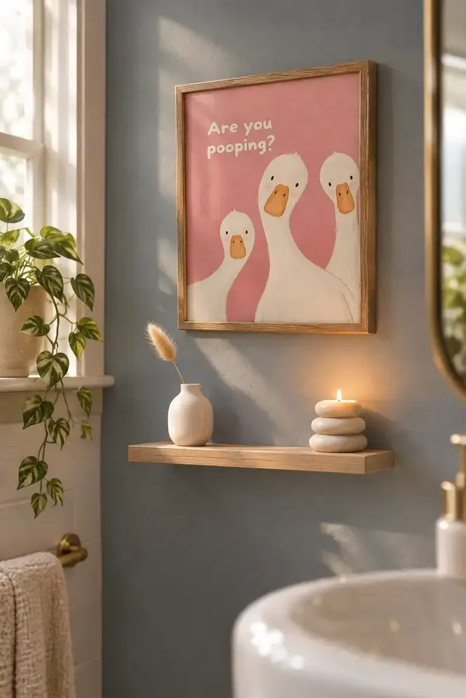 Funny goose wall print hanging on a dusty blue bathroom wall above a birch shelf with minimal dried grass and candle